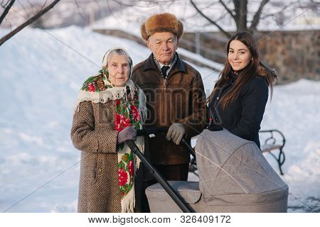 Grand Grandparents Walking With A Baby In Beautiful Pram. Winter Time