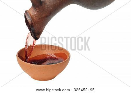 A Red Wine Is Pouring From Traditional Georgian Wine Jug In To The Clay Cup, Isolated White Backgrou
