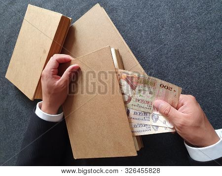 Hands Of A Businessman With Uruguayan Money And Books On The Table