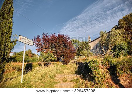 View Of  The Old Town Of Barjac, Southern France. Green Trees, Buildings And Stone Church With A Bel