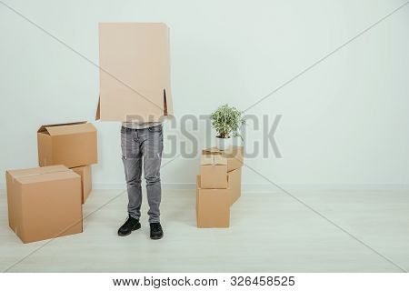 Funny Man Is Standing With Cardboard Box On His Head. Handsome Young Man Moving Into New House.