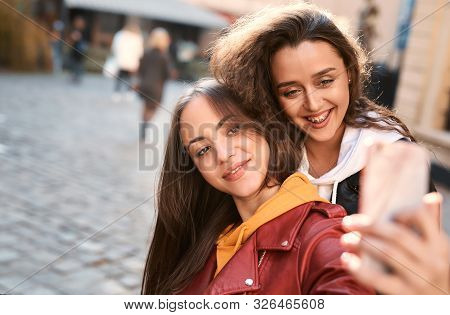 Portrait Of Cute Young Women Smiling And Making Selfie By The Phone Uotdoors In City