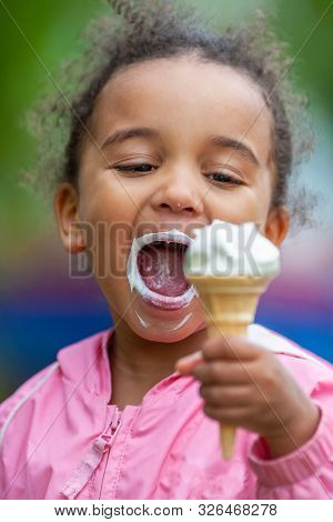 Outdoor portrait of beautiful happy cute, kid, mixed race African American girl female child eating an ice cream cornet with a messy mouth and face