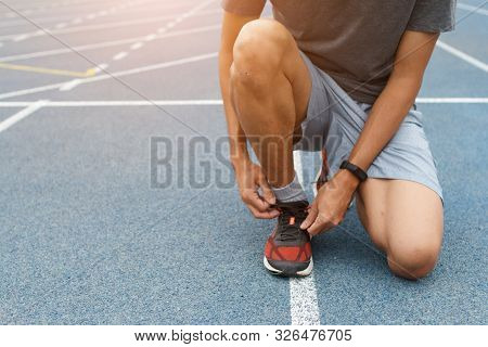Close-up Of Sportsman In Blue Running Track In Stadium. He Tying Sneakers On Running Shoes Before Pr