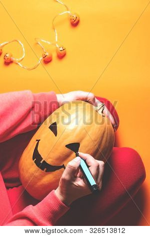 Hands Of A Woman Sitting On Her Knees And Drawing Scary Face On Little Pumpkin With A Black Marker P