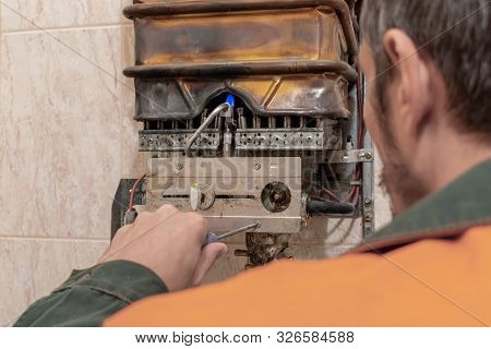 A Worker Performs Maintenance Of An Old Copper Gas Boiler. The View From The Back. The Concept Of Ca