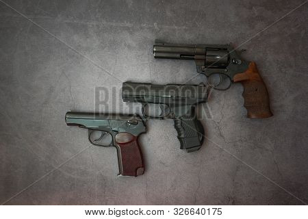 Firearms Laid Out Along The Line. Three Guns Close-up On A Gray Concrete Background. Copy Space.