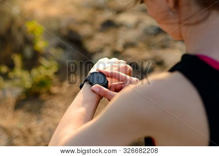 Young Woman Runner Using Multisport Smartwatch at Sunset on the Mountain Trail. Closeup of Hands with Fitness Tracker. Training and Sports Concept.
