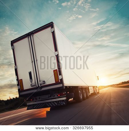 Backview of european truck vehicle on motorway with dramatic sunset light. Cargo transportation and supply theme.