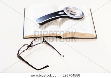 Reading Book With Low Vision - Eyeglasses And Magnifier On Open Book On Pale Table (focus In The For