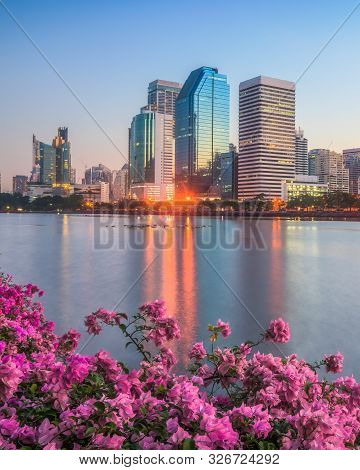Lake With Purple Flowers In City Park Under Skyscrapers At Sunrise. Benjakiti Park In Bangkok, Thail