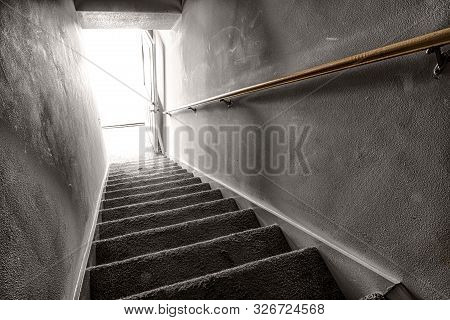 Horizontal Shot Looking Down A Stairway To The Light Coming From An Open Door At The Bottom.