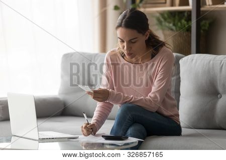 Serious Woman Calculating Domestic Bills Writing Notes At Home