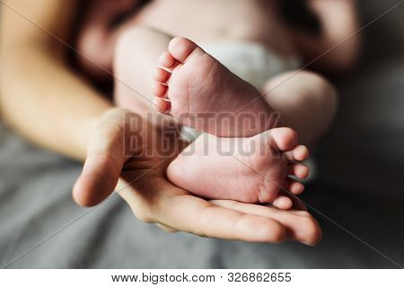 Mother Holding Newborn Baby Feet In Hands. Mom Taking Care About Infant Child After Taking Bath. Par