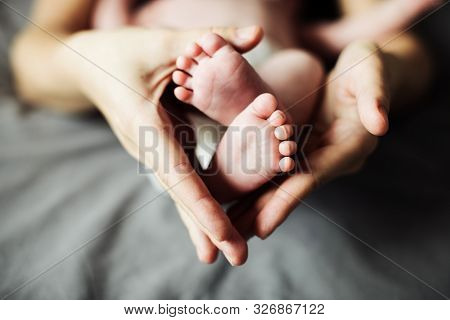 Mother Holding Newborn Baby Feet In Hands. Mom Taking Care About Infant Child After Taking Bath. Par