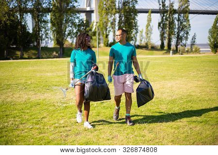 Eco Activists Chatting While Working In City Park. Young Man And Woman Walking On Grass, Talking, Ca