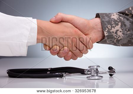 Doctor And A Military Man Shaking Hands Over The Stethoscope On White Table