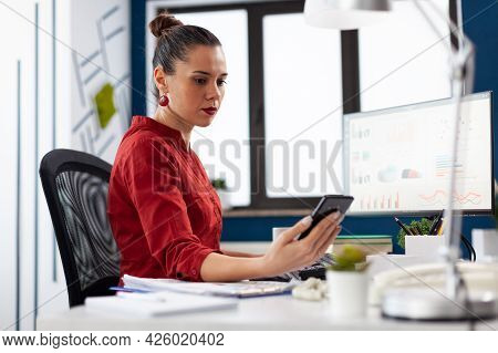 Business Woman Looking At Smartphone Screen Receiving Text Message, While Working On Deadline Projec