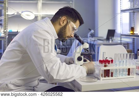 Scientist Looking In Microscope While Doing Research In Biotech Science Laboratory