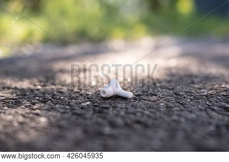 One Wireless Headphones Is Lost And Lies On The Asphalt Sidewalk, Outdoors.