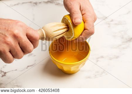 Man Hands Squeezing A Half Lemon With A Wooden Squizzer On A Marble Countertop