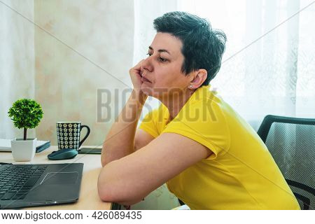 Short-haired, Gray-haired Brunette Woman Rests Her Head On Her Hand While Sitting At A Table In Fron