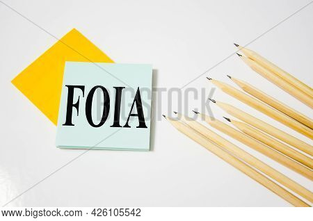Foia Word Written On A Yellow Piece Of Paper And White Background With Pencils Lying Next To It