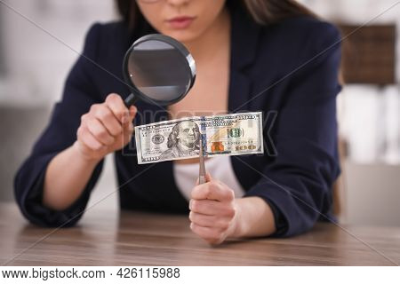 Expert Authenticating 100 Dollar Banknote With Magnifying Glass At Table In Office, Closeup. Fake Mo