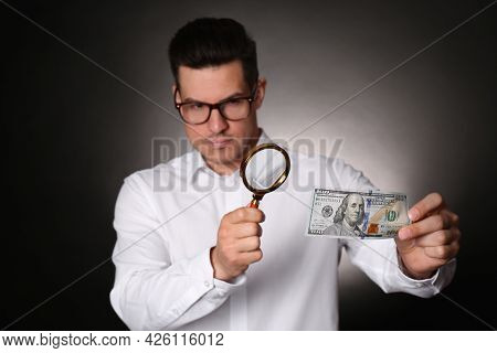 Expert Authenticating 100 Dollar Banknote With Magnifying Glass Against Dark Background, Focus On Ha
