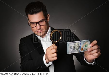 Expert Authenticating 100 Dollar Banknote With Magnifying Glass Against Dark Background. Fake Money 