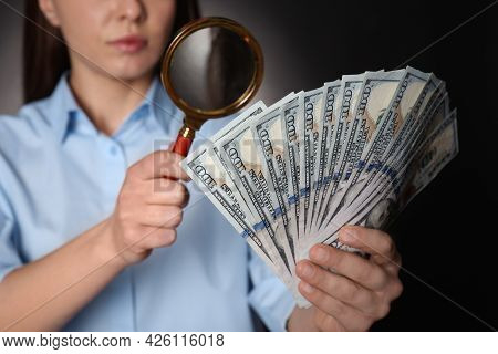 Expert Authenticating 100 Dollar Banknotes With Magnifying Glass Against Dark Background, Closeup. F