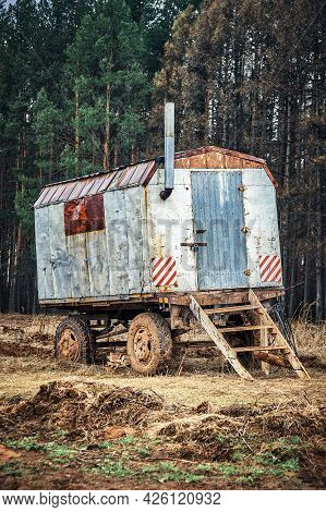 Old Rusty Metal Semi Trailer House With Chimney And Wooden Steps Stands On Field By High Pine Trees 