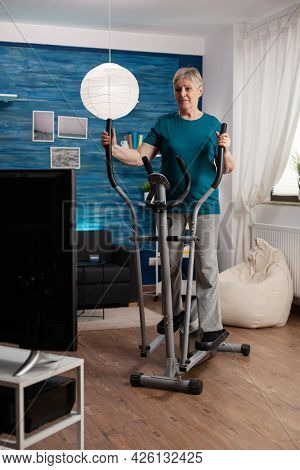 Focused Senior Woman Working At Legs Muscle Resistance Cycling Bicycle Machine In Living Room During