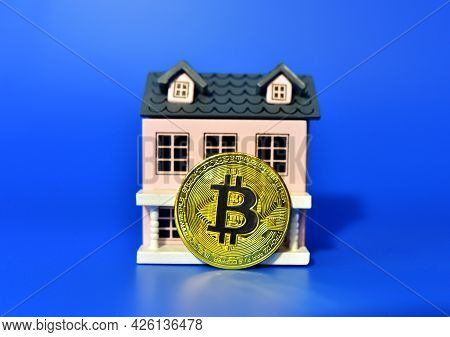 Bitcoin Coin On The Background Of A Wooden House. The Concept Of Buying Real Estate And Housing For 