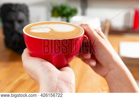 Hands Hold A Cup Of Cappuccino. Drawing In A Cup.