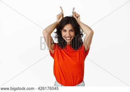 Smiling Coquettish Brunette Woman Holding Fingers On Head, Bull Devil Horns Gesture, Looking Silly A