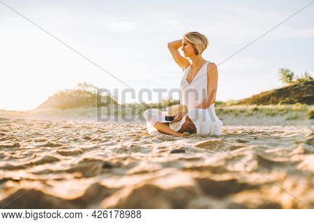 Young Slim Woman Wearing White Long Dress Sit Alone At The Beach Or Ocean Or Sea. Loneliness, Divors