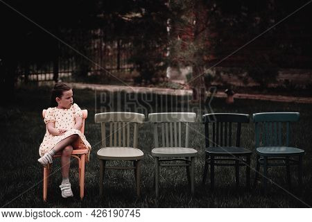 A Lonely, Sad Girl In A Dress Sits On An Empty Row Of Chairs In The Backyard Of The Outdoots And Cri