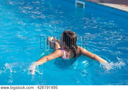 Girl Floating On An Inflatable Circle In The Blue Water Of The Swimming Pool Of The Pool, The Concep
