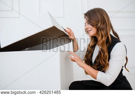 Happy Young Girl With Wavy Hair And In Festive Clothes Opens A Big Gift, Smiling. New Year And Birth
