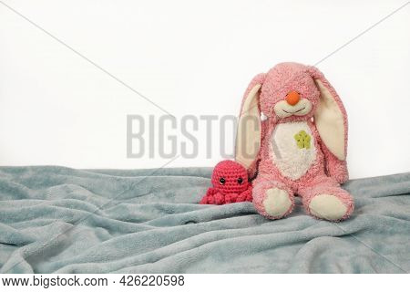 A Plush Bunny Toy Sitting On Plush Blanket And White Wall. Plush Pink Bunny Toy With Pink Knitted Oc