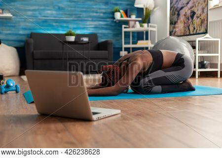 Black Woman Sitting On Yoga Mate Doing Stretching Relaxing Body After Watching Online Training Looki