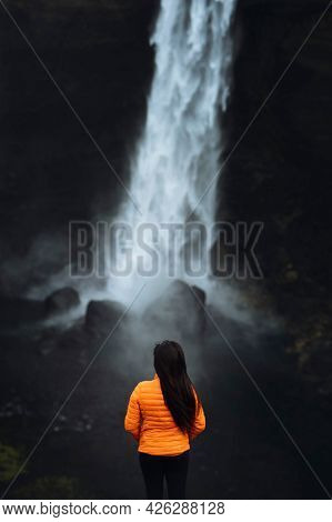Woman in an orange jacket at the Haifoss waterfall, Iceland