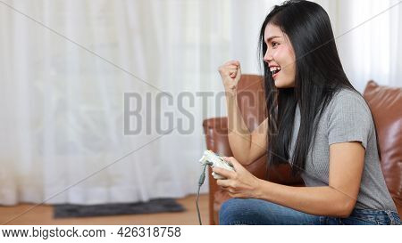 Vdo Game Console Station Concept. Active Asian Woman Sitting On Sofa, Holding Joystick And Playing E