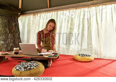 Front View Of A Young Woman Smiling And Working On The Fresh Air , She Is Sitting In Tent On The Red