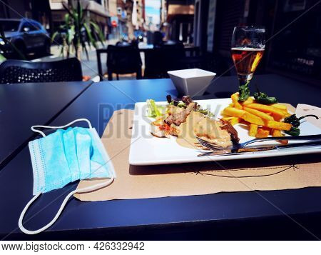 Medical Mask On The Serviced Table. Work Of The Cafes And Restaurants During Covid-19 Pandemic