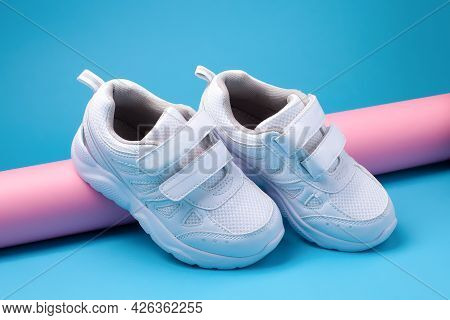 Close-up Of Two White Kid Sneakers With Velcro Fasteners For Easy Footwear On A Pink Long Paper Roll
