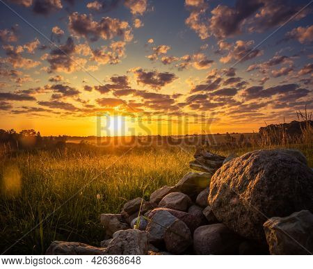 Sunrise Landscape With Roks On The Siede Of The Meadow And Field. Summertime Scenery Of Northern Eur