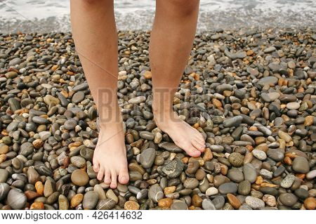 Pebble Beach. Bare Feet Stand On Round Pebbles.