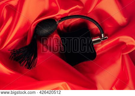 Black Bottle Of Eau De Toilette Or Perfume With Long Tassel Spray Pomp Lies On Red Background Of Flo